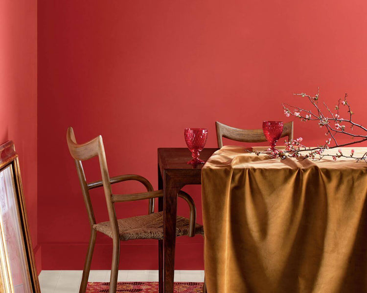 dining room with coral tinged with pink painted wall, a table, chairs, cups and branch with buds